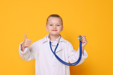 Photo of Little girl with stethoscope pretending to be doctor on orange background. Dreaming of future profession