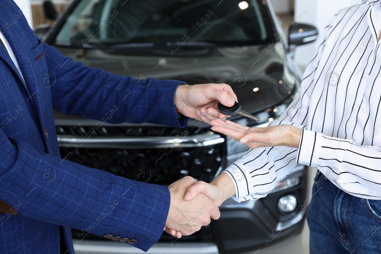 Photo of Salesman giving key to client near new car in salon, closeup