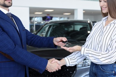 Photo of Salesman giving key to client near new car in salon, closeup