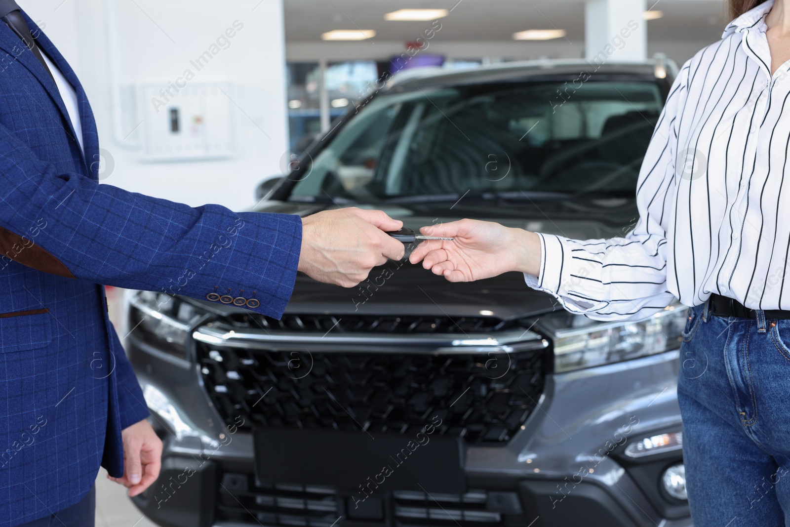 Photo of Salesman giving key to client near new car in salon, closeup