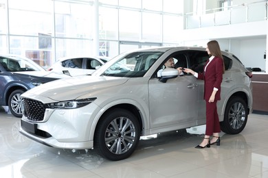 Photo of Happy saleswoman and client inside new silver car in salon