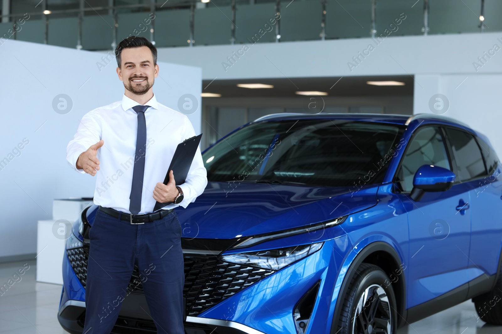 Photo of Happy salesman reaching for handshake with client near new blue car in salon