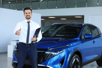 Photo of Happy salesman reaching for handshake with client near new blue car in salon