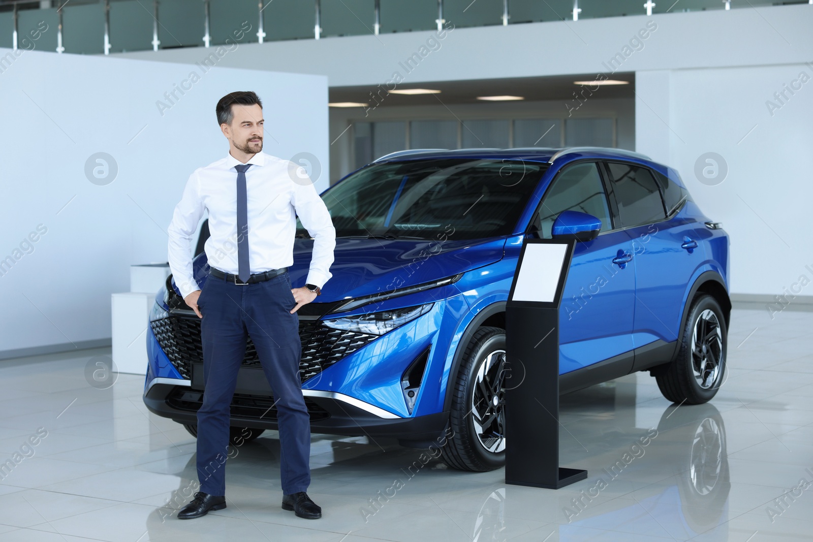 Photo of Happy salesman near new blue car in salon