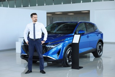 Happy salesman near new blue car in salon