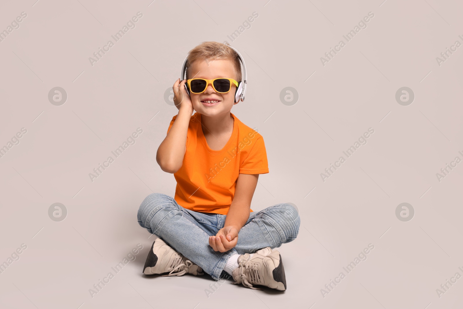 Photo of Little boy with sunglasses listening to music on light grey background