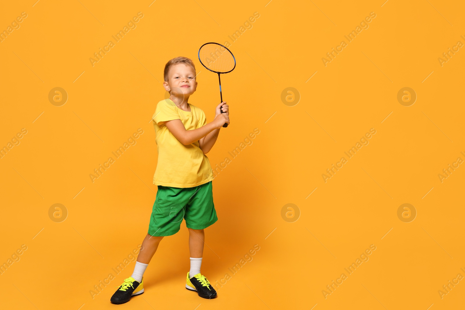 Photo of Little boy with badminton racket on orange background, space for text