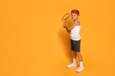 Photo of Little boy with badminton racket on orange background, space for text