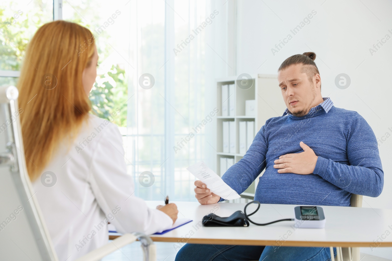 Photo of Nutritionist consulting overweight man at table in clinic