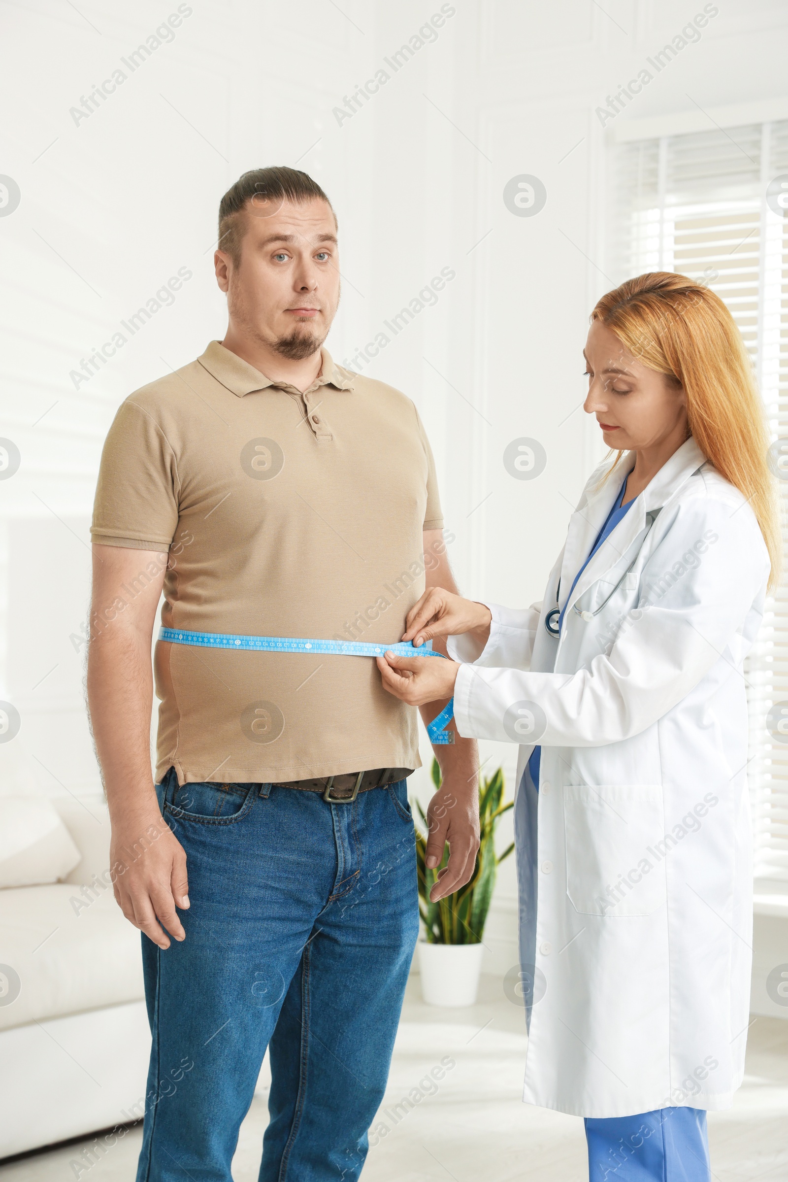 Photo of Nutritionist measuring overweight man's waist with tape in clinic