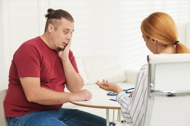 Photo of Overweight man having consultation with nutritionist at table in clinic