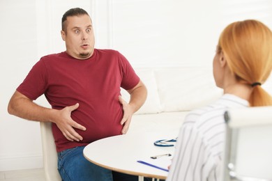 Photo of Overweight man having consultation with nutritionist at table in clinic