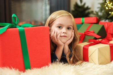 Photo of Little girl with Christmas gifts on floor at home