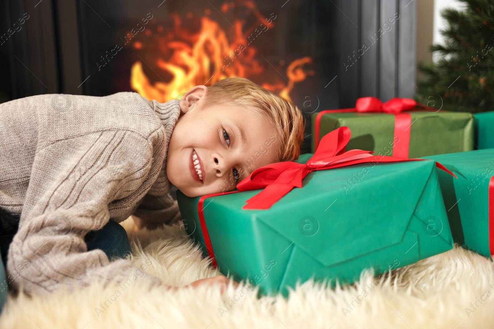 Photo of Little boy with Christmas gifts on floor at home