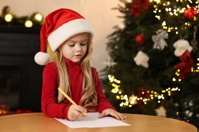 Photo of Little girl writing letter to Santa Claus at table indoors. Christmas celebration