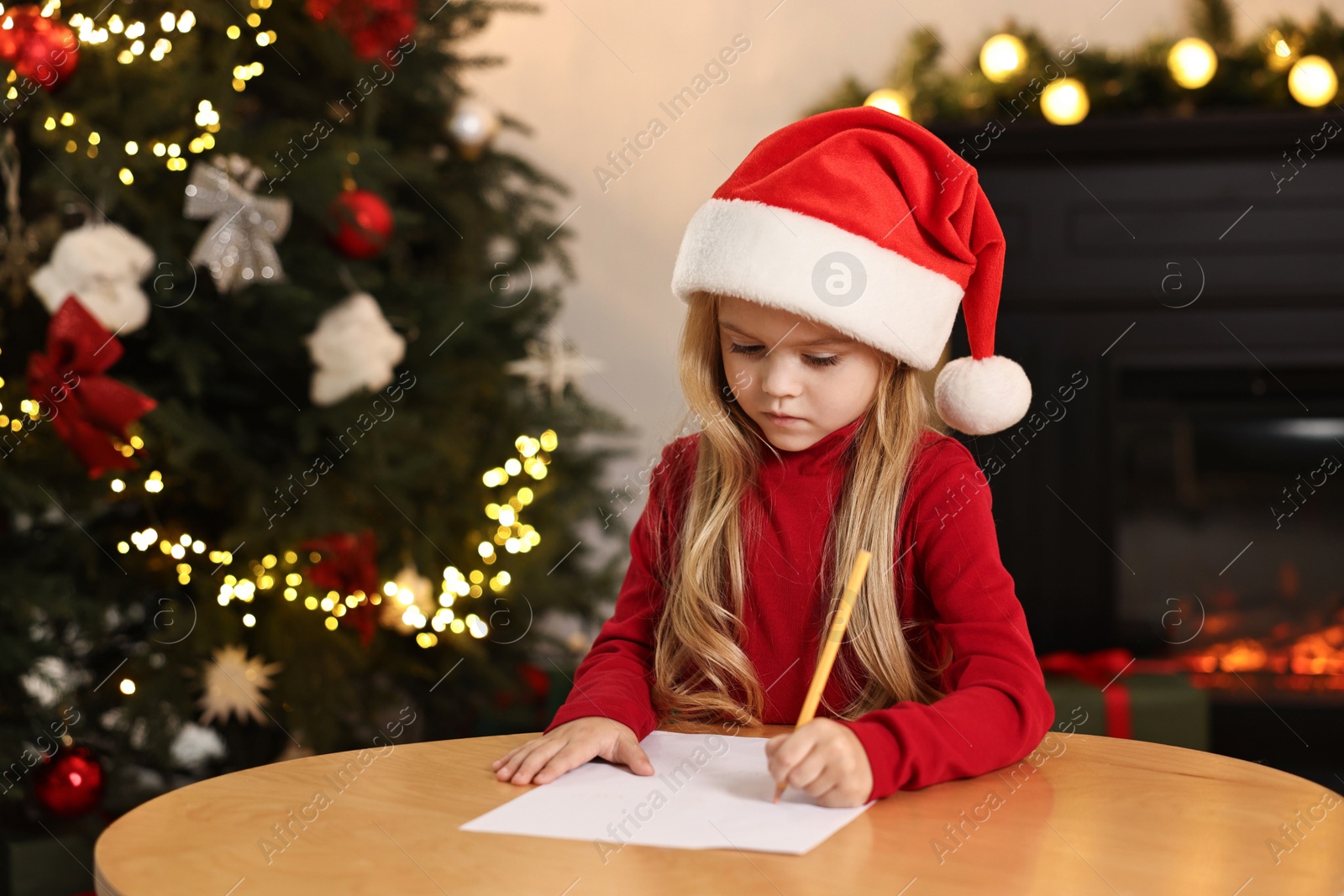 Photo of Little girl writing letter to Santa Claus at table indoors. Christmas celebration