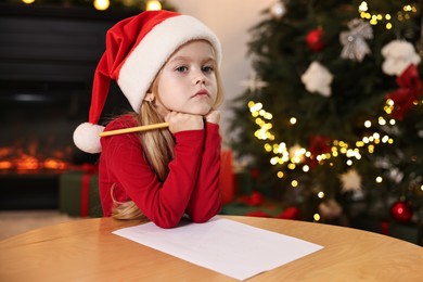 Photo of Little girl writing letter to Santa Claus at table indoors. Christmas celebration