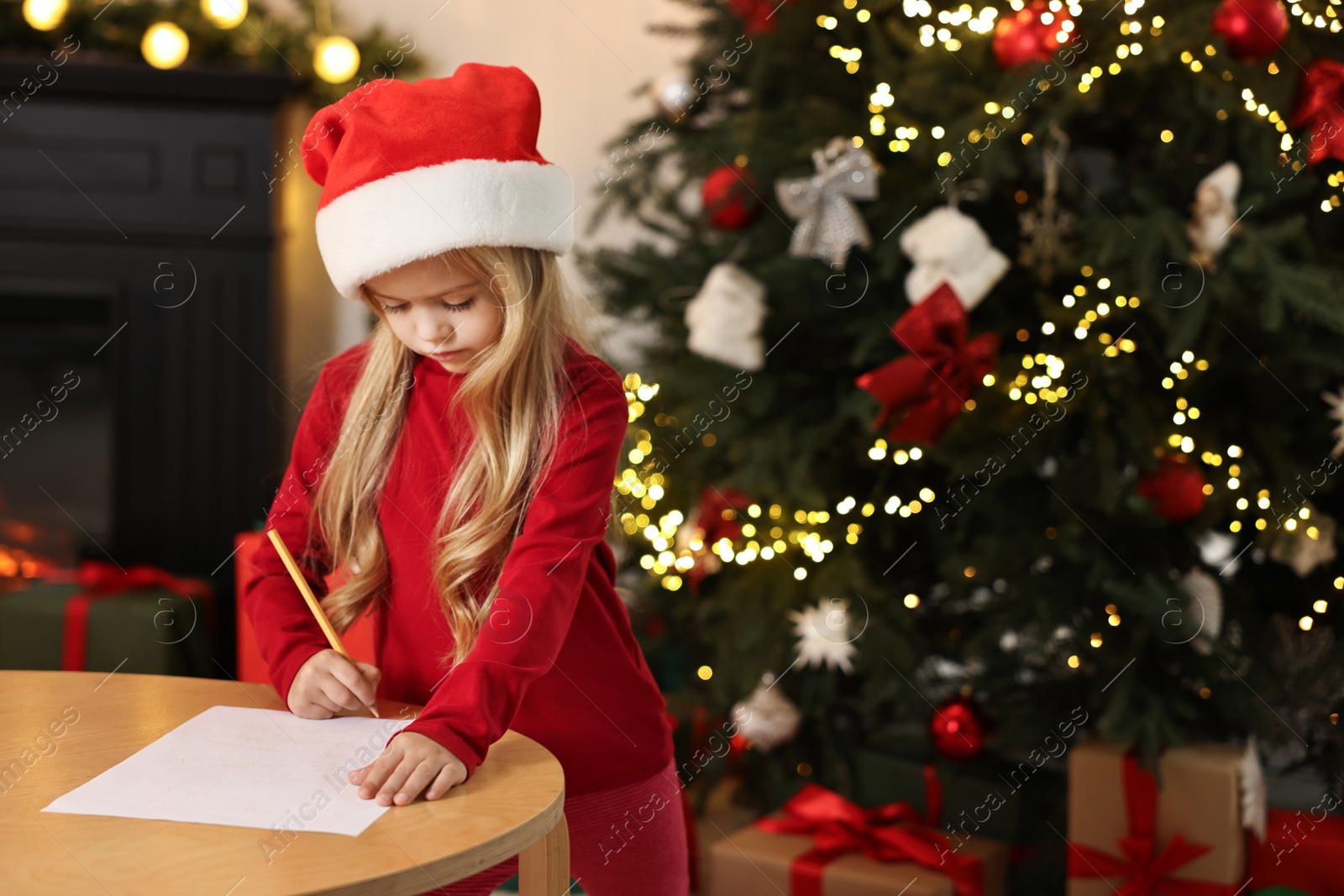 Photo of Little girl writing letter to Santa Claus at table indoors. Christmas celebration