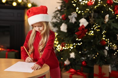 Photo of Little girl writing letter to Santa Claus at table indoors. Christmas celebration