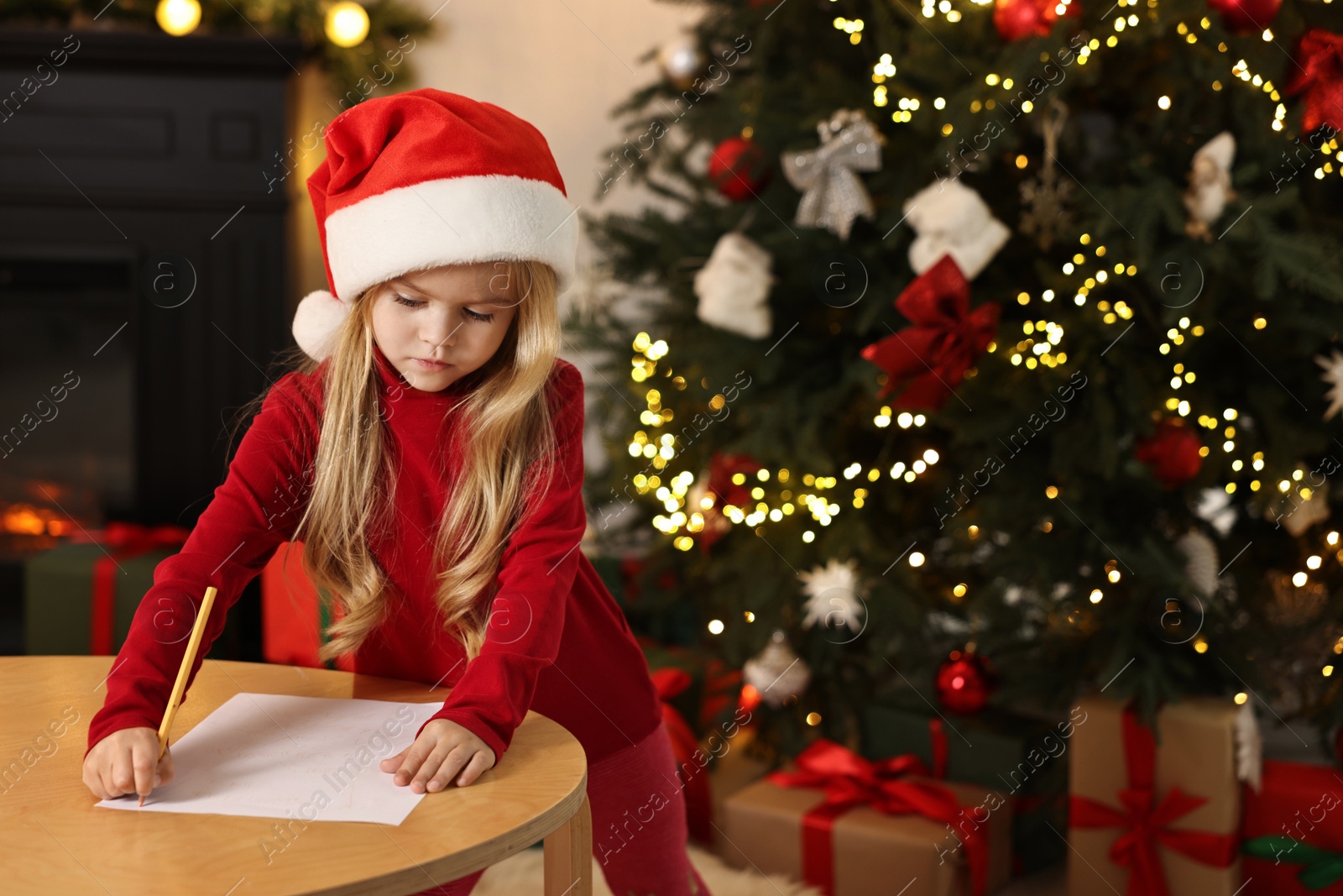 Photo of Little girl writing letter to Santa Claus at table indoors. Christmas celebration