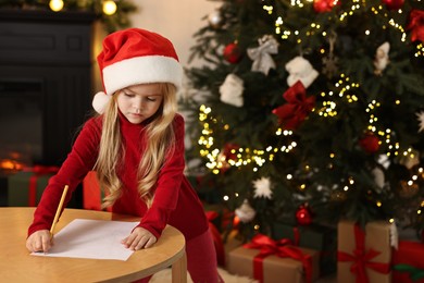 Photo of Little girl writing letter to Santa Claus at table indoors. Christmas celebration