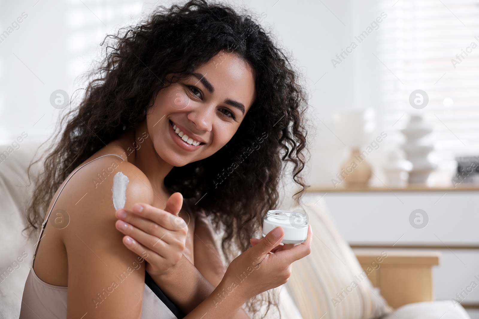 Photo of Beautiful woman applying cream onto shoulder at home. Space for text