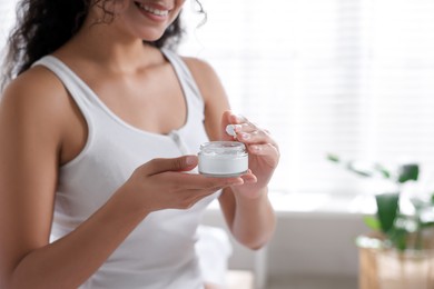 Woman with jar of cream at home, closeup. Space for text