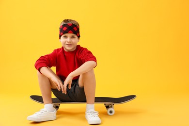 Photo of Little boy with skateboard on yellow background, space for text