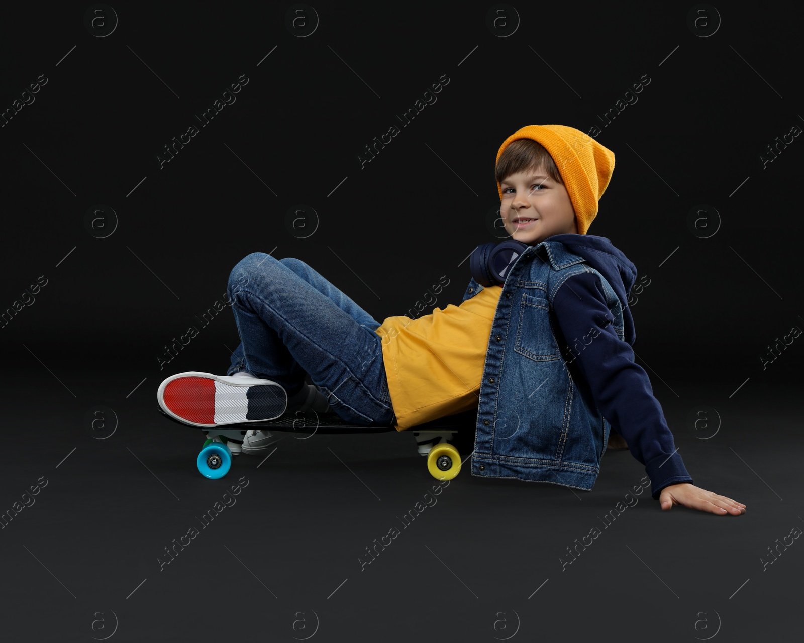 Photo of Little boy with skateboard on black background, space for text