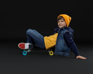 Photo of Little boy with skateboard on black background, space for text