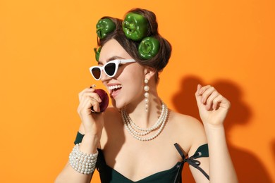 Photo of Young woman with peppers in her hair, sunglasses and onion on orange background