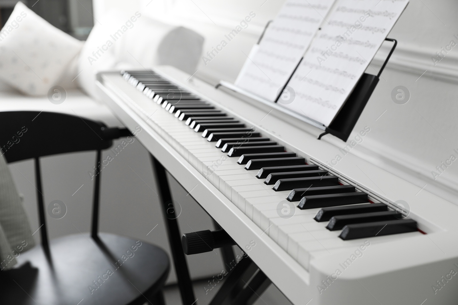 Photo of Synthesizer with music sheets and chair at home, closeup