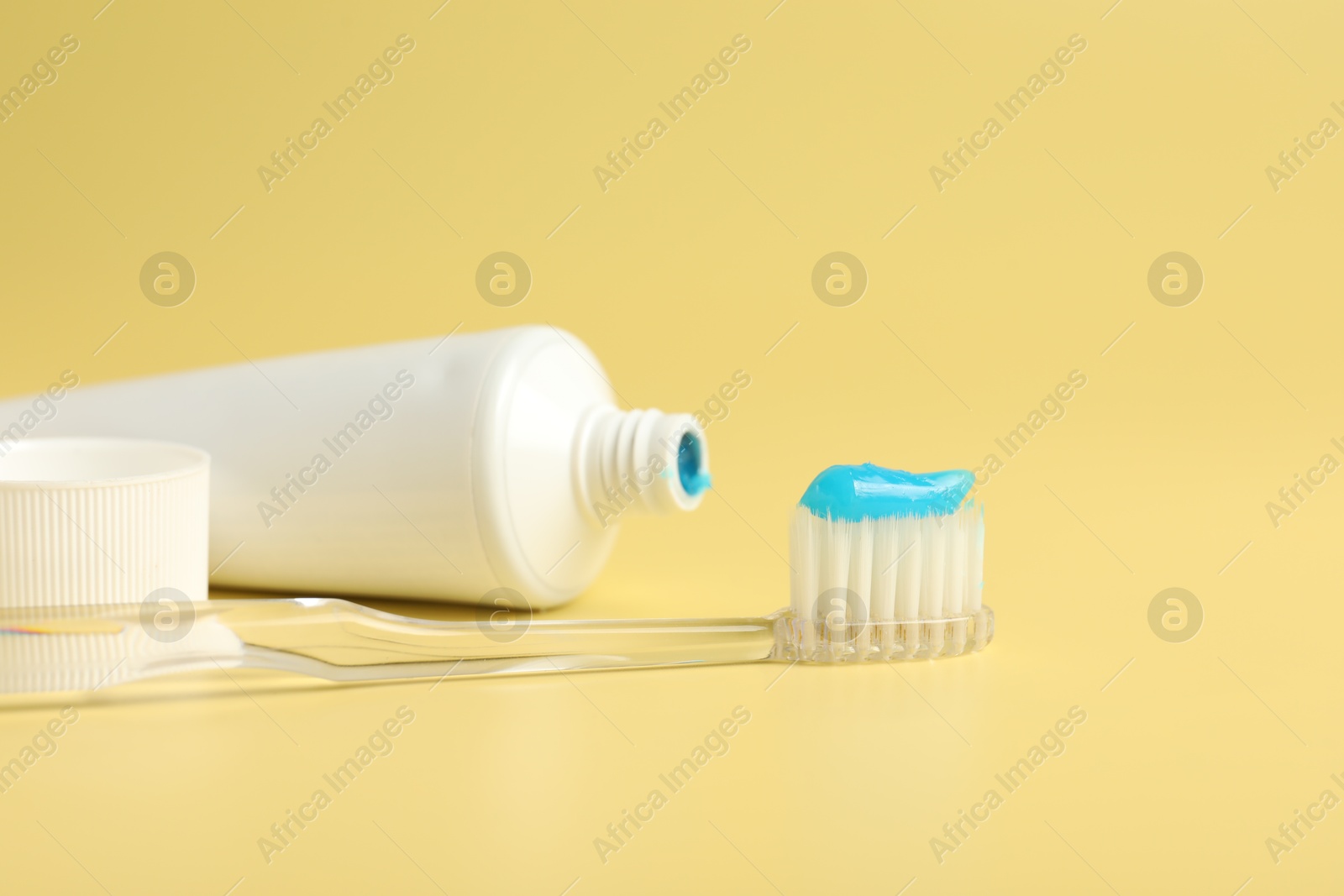 Photo of Toothbrush with toothpaste and tube on yellow background, closeup