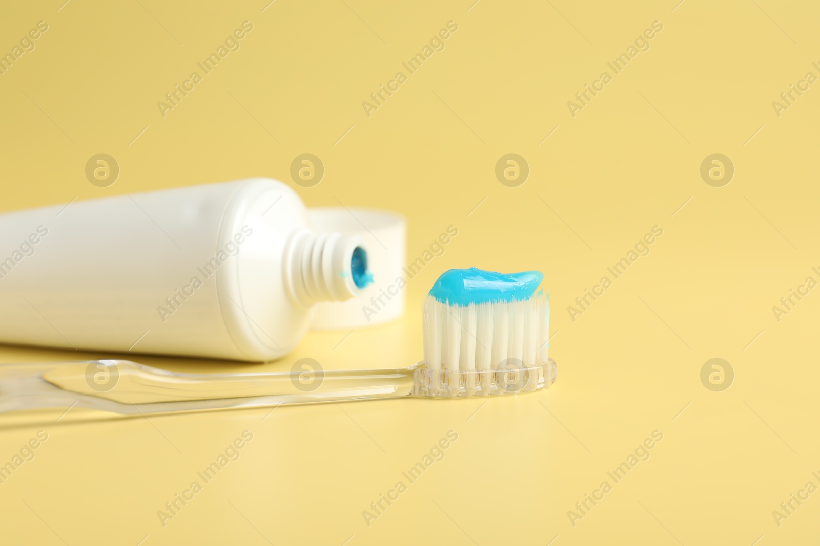 Photo of Toothbrush with toothpaste and tube on yellow background, closeup. Space for text