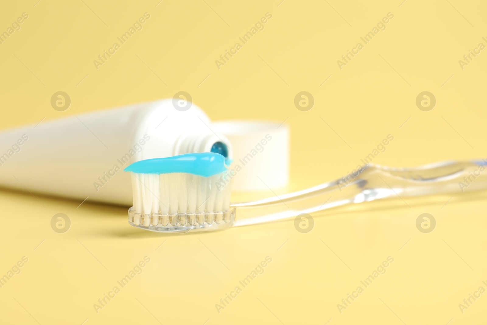 Photo of Toothbrush with toothpaste and tube on yellow background, closeup