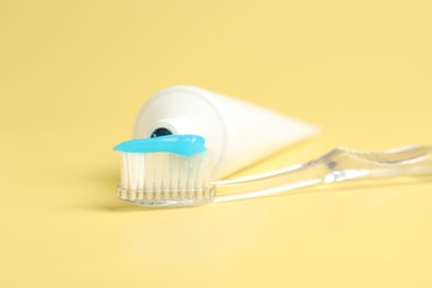 Photo of Toothbrush with toothpaste and tube on yellow background, closeup