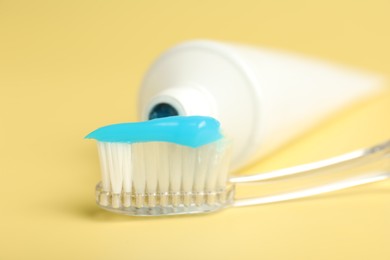 Photo of Toothbrush with toothpaste and tube on yellow background, closeup