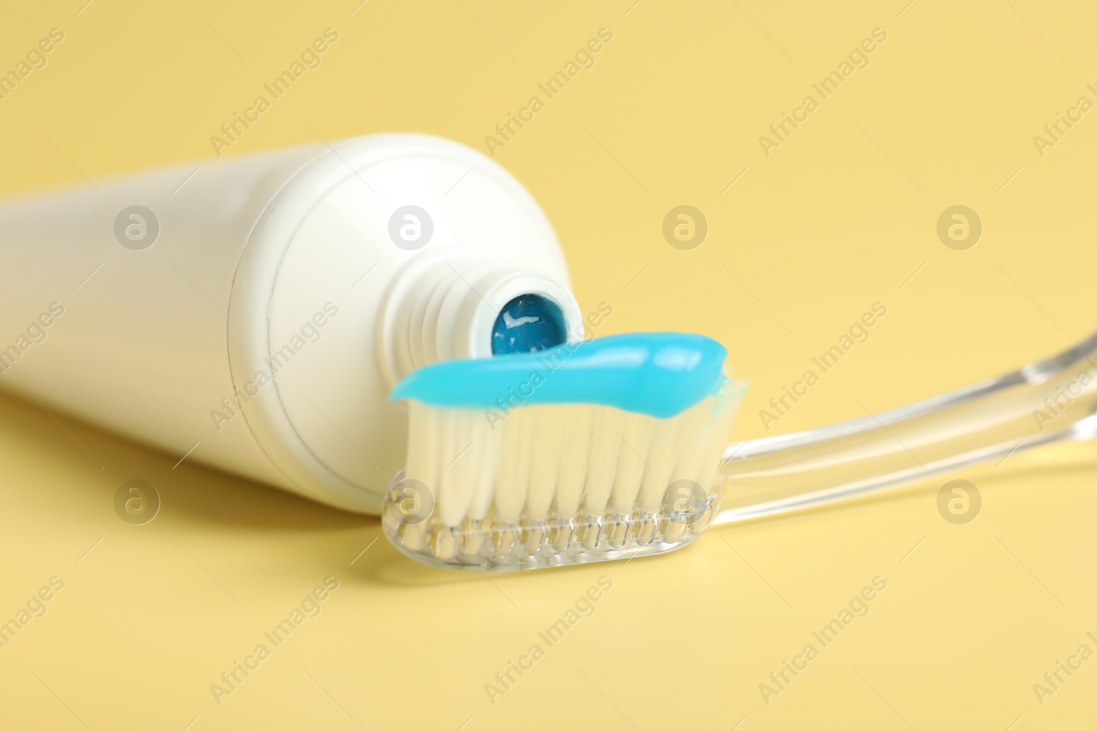 Photo of Toothbrush with toothpaste and tube on yellow background, closeup