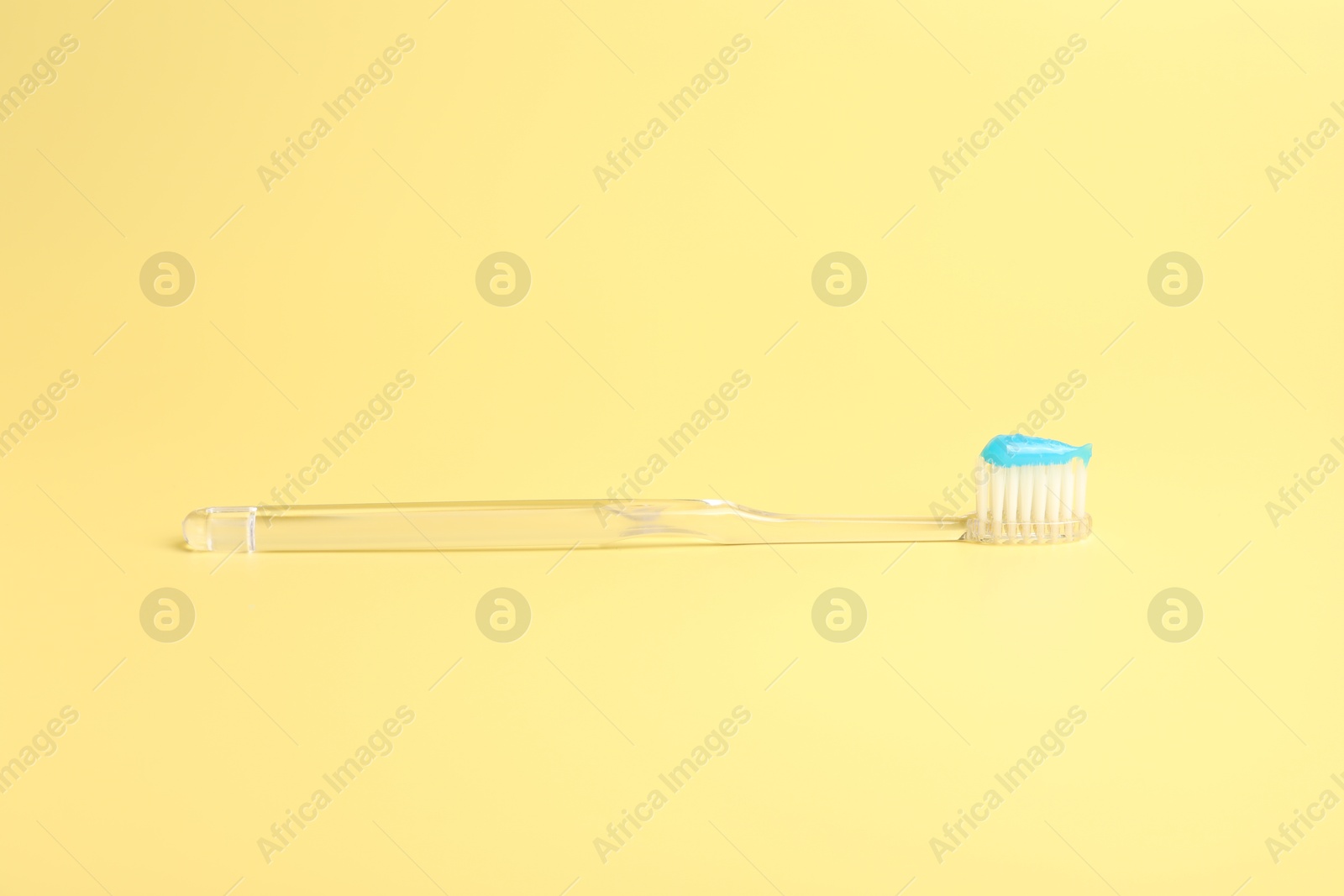 Photo of One toothbrush with toothpaste on yellow background