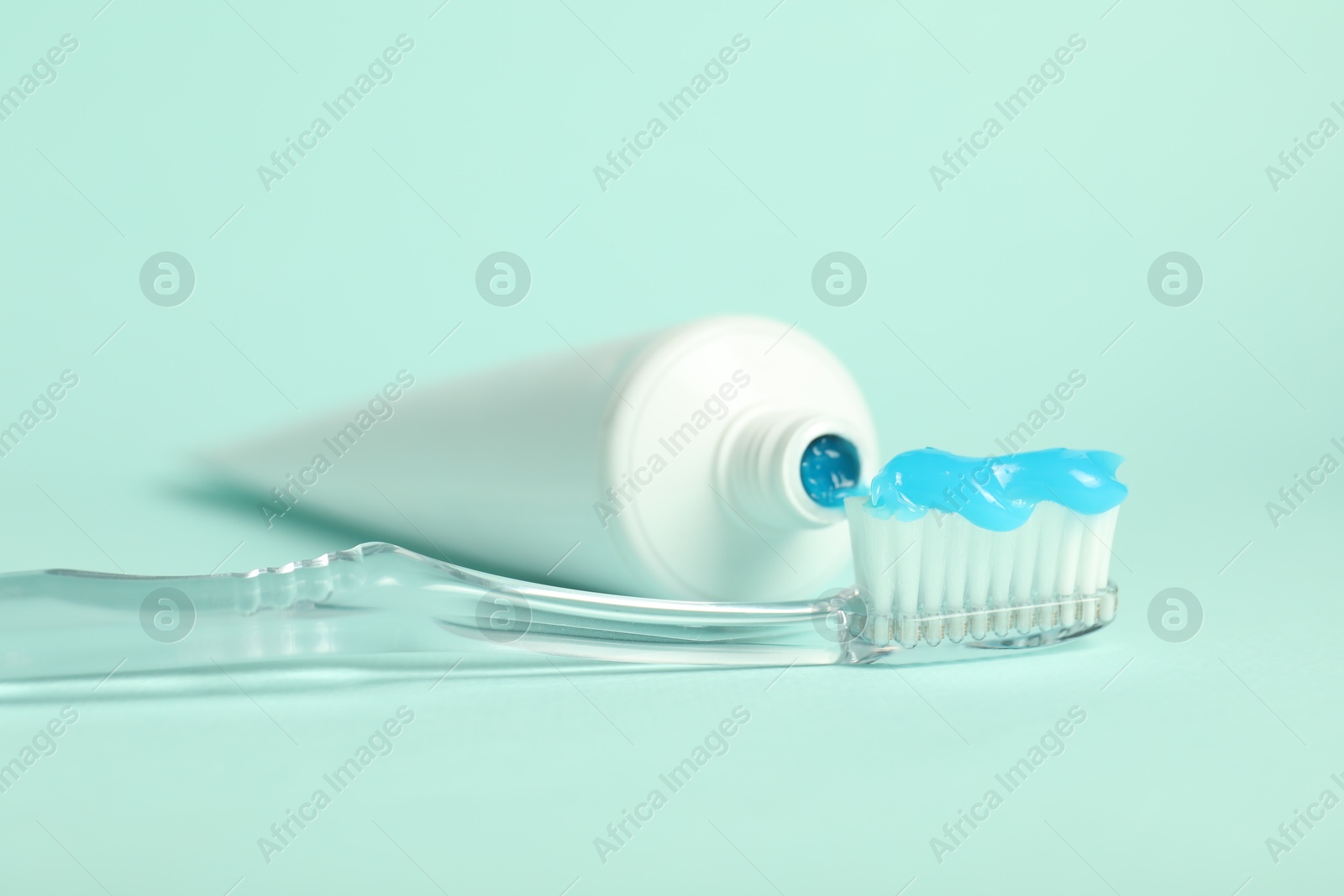 Photo of Toothbrush with toothpaste and tube on light blue background, closeup