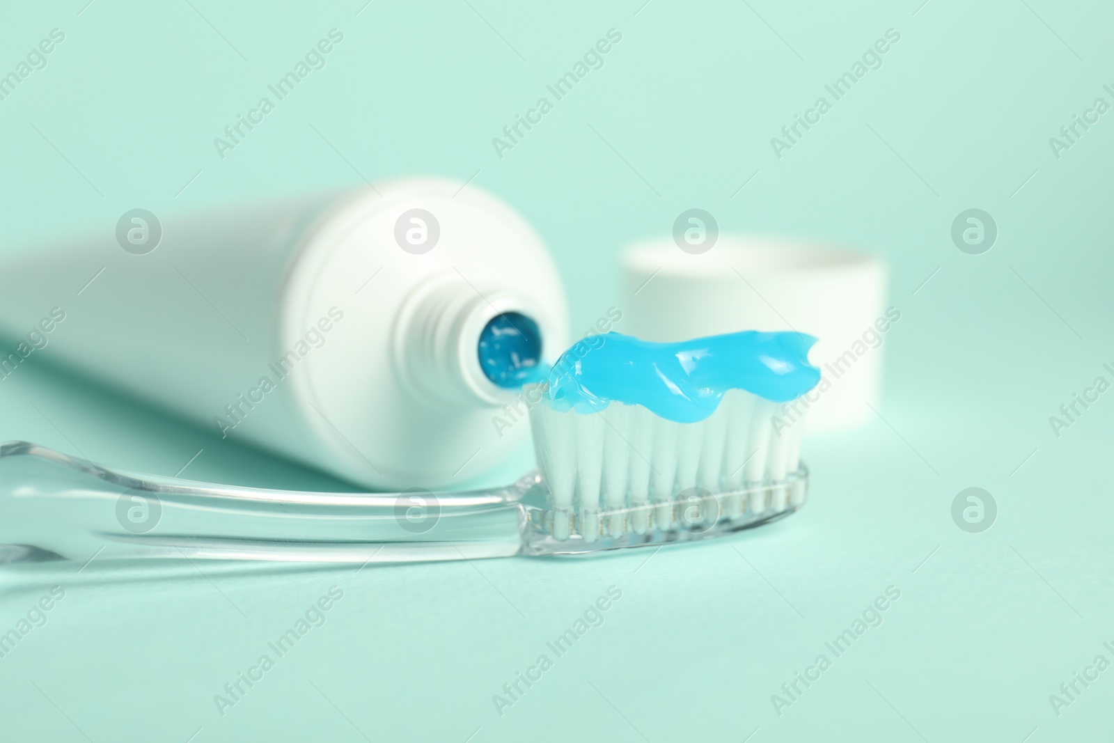 Photo of Toothbrush with toothpaste and tube on light blue background, closeup