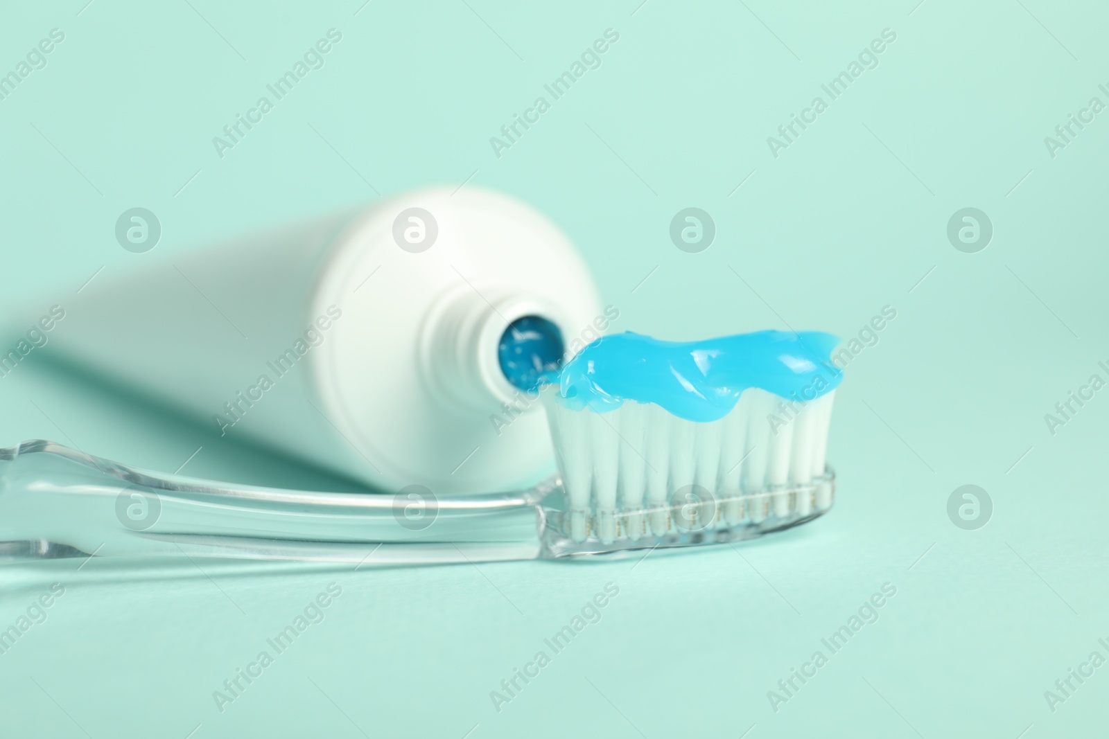 Photo of Toothbrush with toothpaste and tube on light blue background, closeup