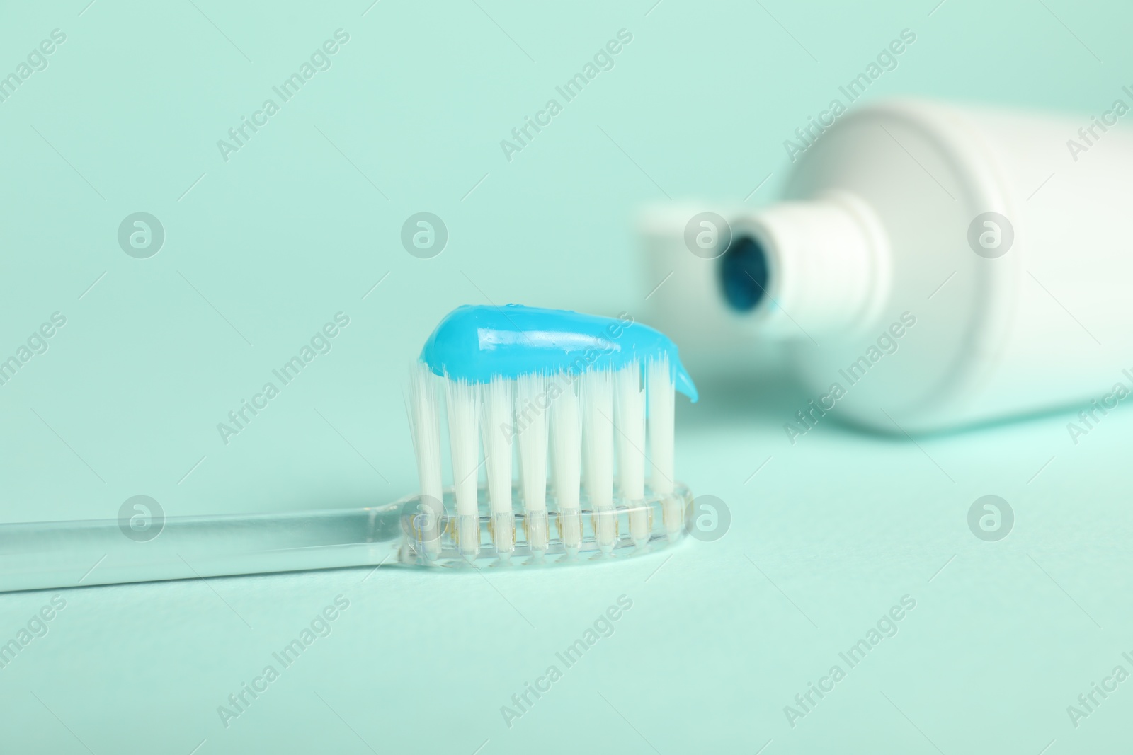 Photo of Toothbrush with toothpaste and tube on light blue background, closeup