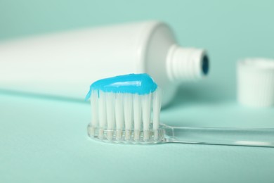 Photo of Toothbrush with toothpaste and tube on light blue background, closeup