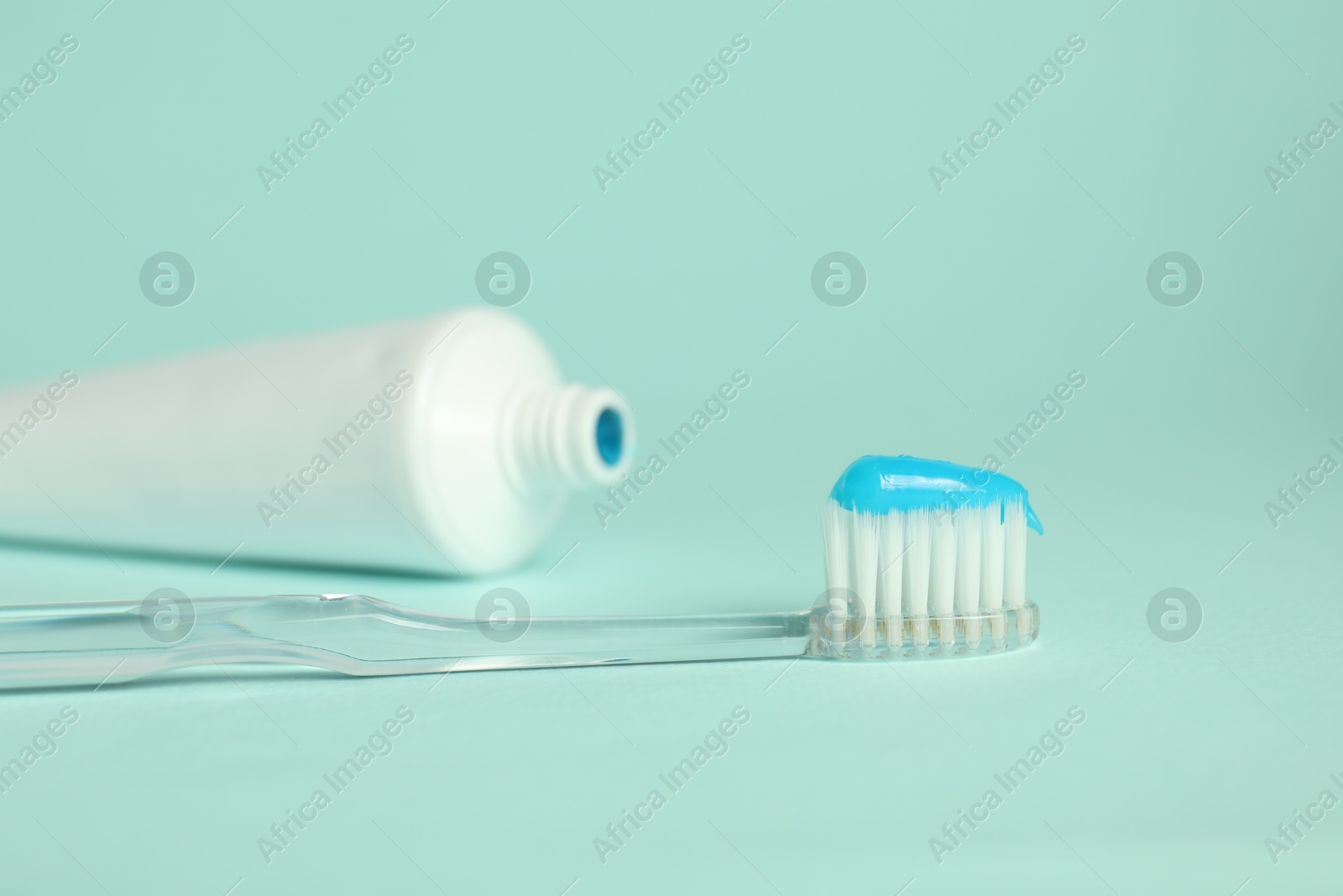 Photo of Toothbrush with toothpaste and tube on light blue background, closeup