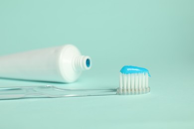 Photo of Toothbrush with toothpaste and tube on light blue background, closeup