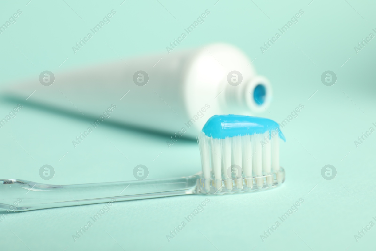 Photo of Toothbrush with toothpaste and tube on light blue background, closeup