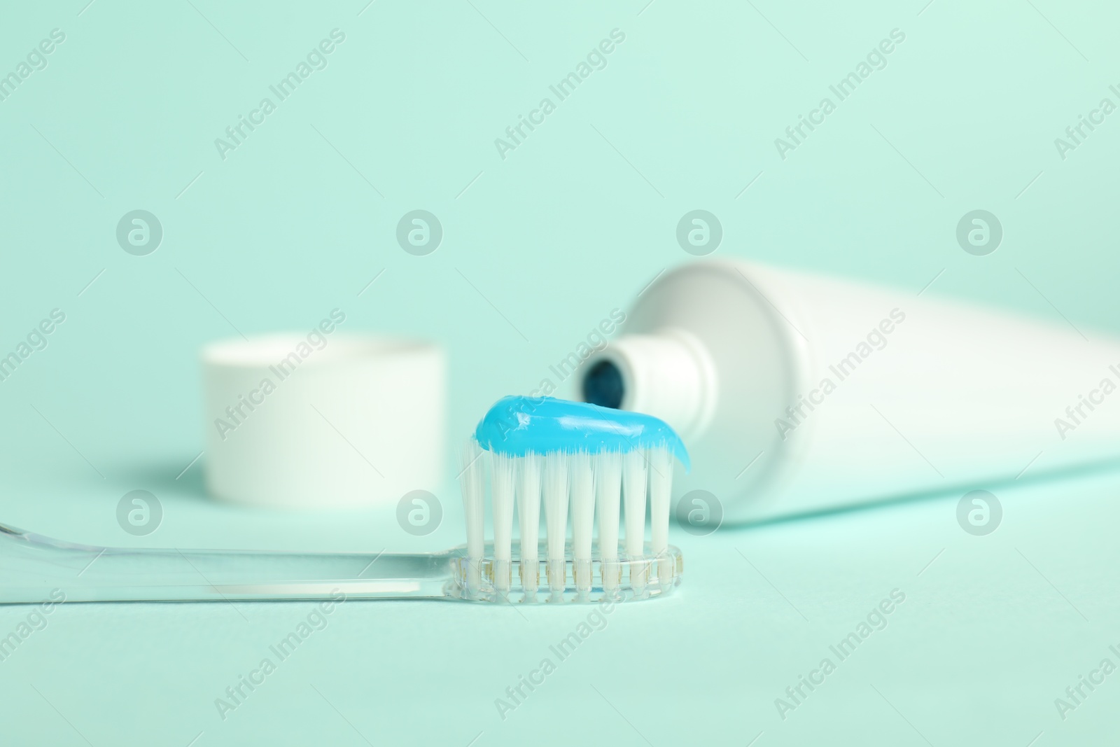 Photo of Toothbrush with toothpaste and tube on light blue background, closeup