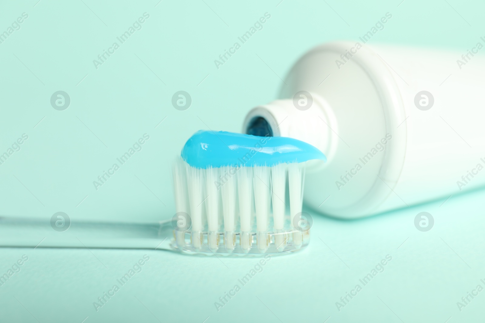 Photo of Toothbrush with toothpaste and tube on light blue background, closeup