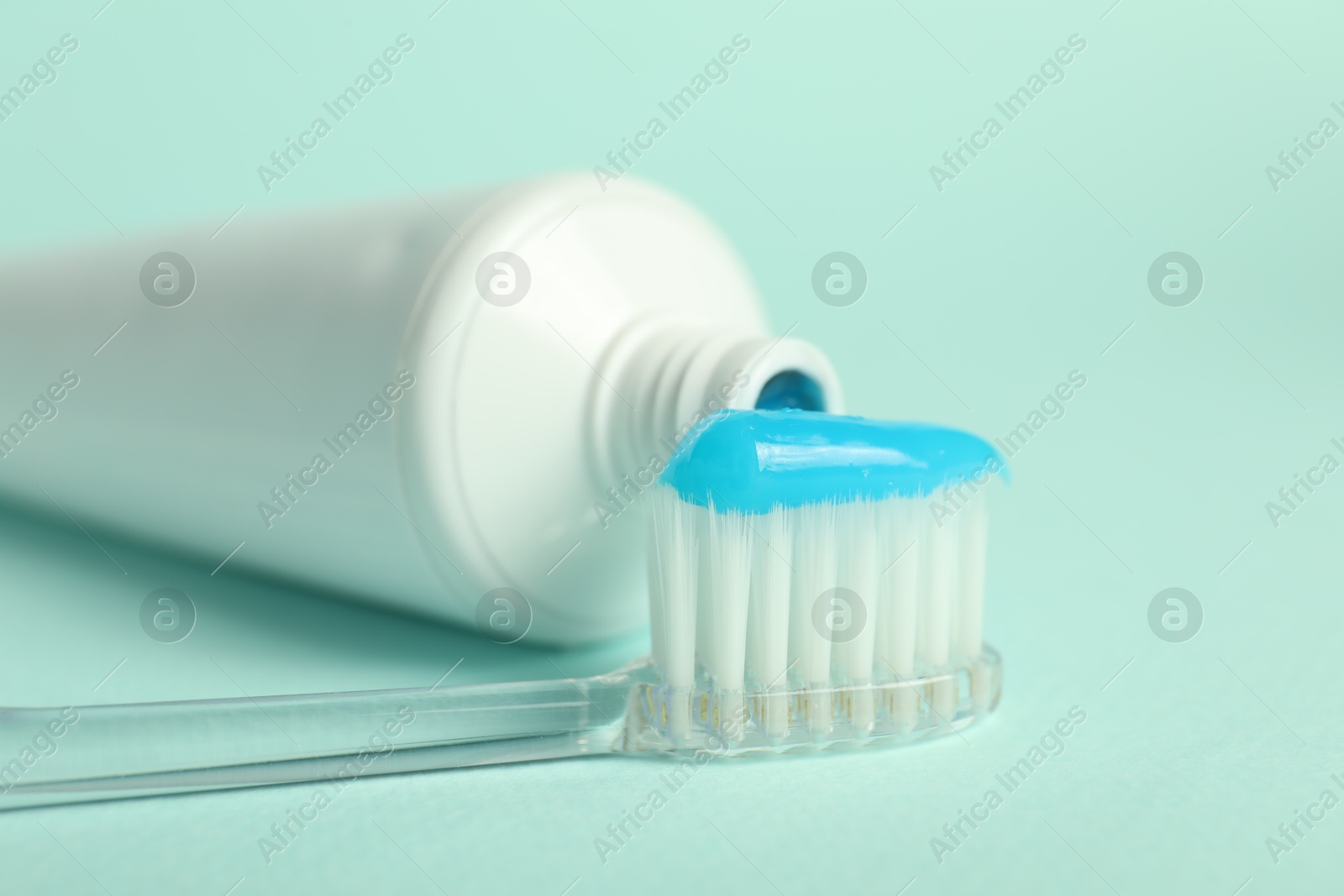 Photo of Toothbrush with toothpaste and tube on light blue background, closeup